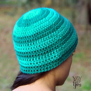 May include: A teal and green crocheted beanie hat. The hat is made with a simple stitch pattern and has a slouchy fit.
