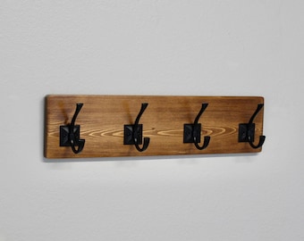 May include: A wooden coat rack with four black metal hooks. The rack is stained a dark brown color.