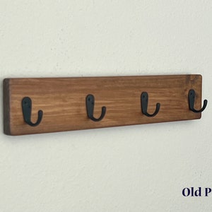 May include: A wooden wall-mounted coat rack with four black metal hooks. The wood is stained a dark brown color and labeled "Old Pine".