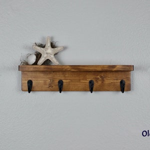 May include: A wooden shelf with four black hooks, stained in an Old Pine finish. A starfish and a seashell are on the shelf.