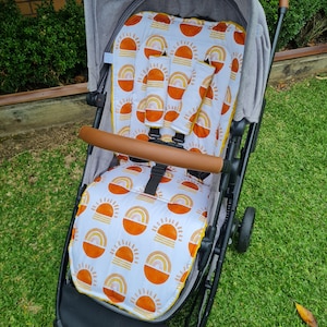 May include: A stroller with a white, orange, and yellow sun and rainbow patterned seat liner. The stroller has a gray canopy and black frame.