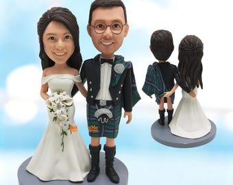 May include: A custom bobblehead figurine set featuring a couple in wedding attire. The figure on the left wears a white off-the-shoulder gown and holds a white bouquet. The figure on the right wears a black jacket, white shirt, bow tie, and a green and blue plaid kilt with black boots.