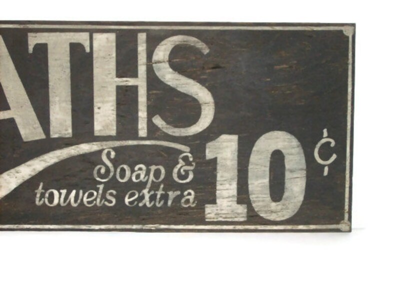 May include: A vintage wooden sign with white painted lettering advertising "BATHS 10&cent;" with the text "Soap & towels extra" below. The sign has a rustic, weathered look.