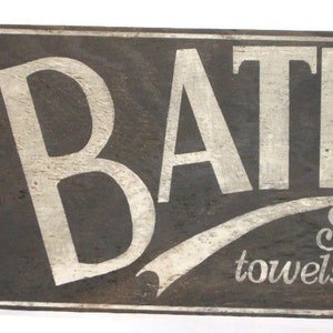 May include: A vintage wooden sign with white painted lettering that reads "BATH" with a white painted flourish underneath that says "Soap, towels etc."