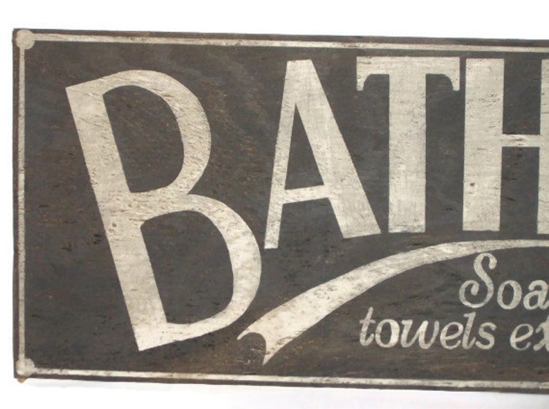 May include: A vintage wooden sign with white painted lettering that reads "BATH" with a white painted flourish underneath that says "Soap, towels etc."
