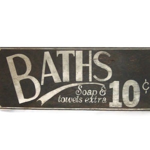 May include: A vintage wooden sign with white lettering advertising baths for 10 cents. The sign reads "BATHS Soap & towels extra 10&cent;".