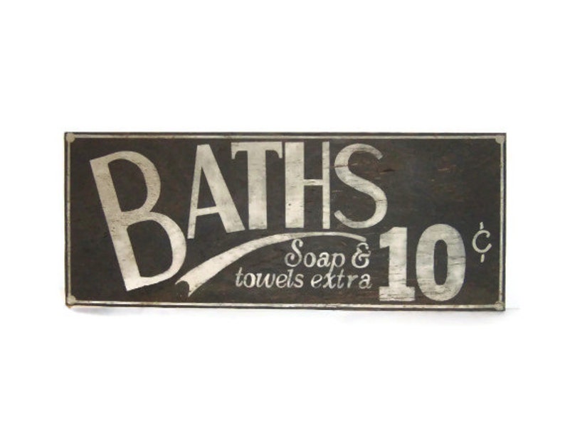 May include: A vintage wooden sign with white lettering advertising baths for 10 cents. The sign reads "BATHS Soap & towels extra 10&cent;".