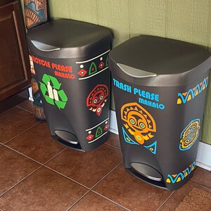 May include: Two black trash cans with colorful Polynesian-inspired designs. The left can says "Recycle Please Mahalo" and has a green recycling symbol. The right can says "Trash Please Mahalo".