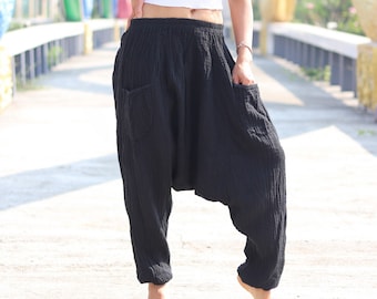May include: A woman wearing a white crop top and black harem pants stands on a bridge. The bridge has colorful arches in the background.