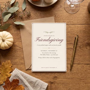 Op de afbeelding: Een rechthoekige Friendsgiving-uitnodigingskaart van crèmekleurig papier met donkerbruine tekst. De kaart luidt: You're invited to Friendsgiving, a cozy potluck supper with our favorite people, Saturday, November 21, Six o'clock in the evening, The Miller Home - 124 Oak Lane, Bring a dish to share and a big appetite, RSVP to Jess by November 14.