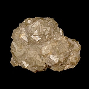 May include: A cluster of light brown, translucent, faceted crystals. The crystals are arranged in a random, organic pattern. The crystals are set against a black background.
