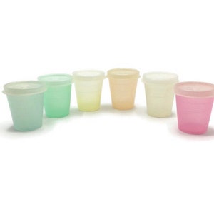 May include: A collection of six small, translucent plastic cups in pastel colors: light blue, green, yellow, peach, white, and pink. Each cup has a matching lid. The cups are arranged in a row against a white background.