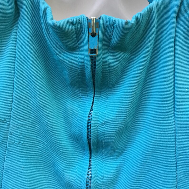 May include: A close-up of a turquoise blue fabric with a silver zipper running down the center.