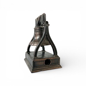 May include: A bronze-colored pencil sharpener shaped like the Liberty Bell. The bell is suspended within a frame, resting on a rectangular base with a pencil-sized hole. The words "Liberty Bell" are visible on the bell.