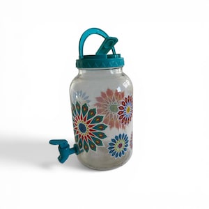 May include: A clear glass beverage dispenser with a teal lid, handle, and spigot. The dispenser is decorated with colorful floral patterns in red, blue, and green. The dispenser is designed to hold liquids and has a capacity of approximately 1 gallon.