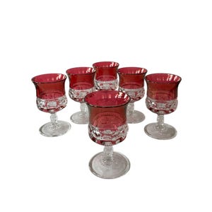 May include: Set of six vintage wine glasses. Each glass features a ruby red bowl and a clear, patterned base. The glasses have a classic design, perfect for serving wine or other beverages. The stemware is ideal for a formal dinner setting.