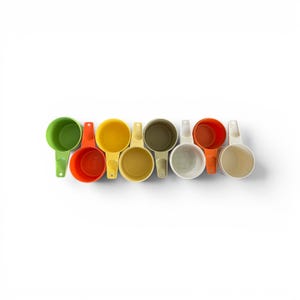 May include: A collection of colorful measuring cups in various shades of green, orange, yellow, and beige. Each cup has a handle and is arranged in a row against a white background. These kitchen tools are designed for measuring dry and liquid ingredients.