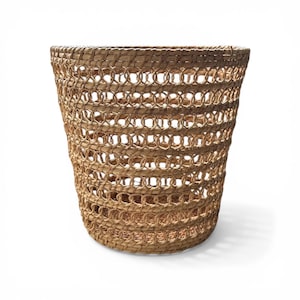 May include: A woven basket with a cylindrical shape. The basket is made of natural-colored fibers, with a pattern of open circles creating a textured appearance. The basket is suitable for storage or decorative use.