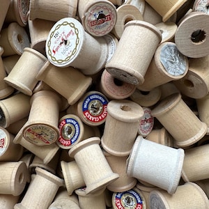 May include: A close-up of a pile of wooden spools of thread. The spools are mostly white with some brown and have various labels on them, including "Coats & Clarks" and "Boilfast".