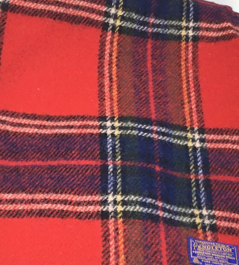 May include: Red plaid Pendleton wool blanket with a blue label that reads "Pendleton Woolen Mills, Portland, Oregon, USA, Pure Virgin Wool".