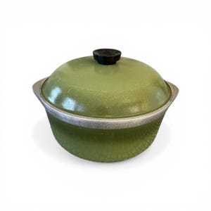 May include: A vintage green cooking pot with a lid. The pot has a textured exterior and a silver rim. The lid is a matching green with a black knob. The pot is designed for cooking and food preparation.