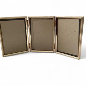 May include: A gold-toned triple picture frame with a beaded border. The frame is open and ready to display three photos.