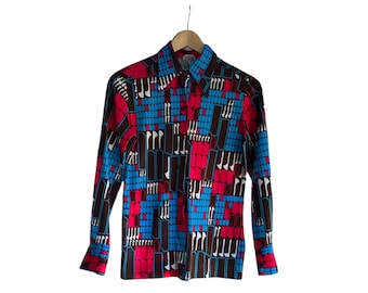May include: A long-sleeved button-down shirt with a vibrant geometric pattern in red, blue, and brown. The shirt is hanging on a wooden hanger against a white background. The pattern consists of rectangular and vertical shapes.