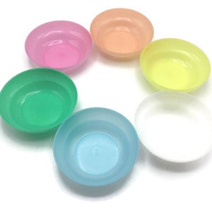 May include: Six small, colorful plastic bowls in a circle on a white background. The bowls are in shades of pink, orange, yellow, green, blue, and white.