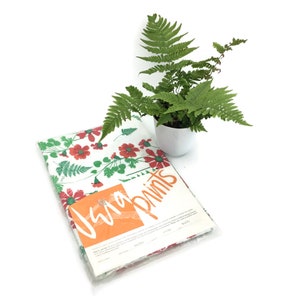 May include: A white tablecloth with a red and green floral pattern. The tablecloth is folded and packaged with a label that reads "Vera Prints".