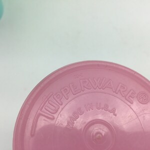 May include: Close-up of the bottom of a pink plastic container with the words "Tupperware" and "Made in U.S.A." embossed on the bottom.