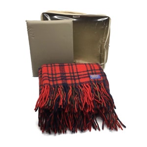 May include: A red and black plaid throw blanket with fringe. The blanket is folded and stored in a beige canvas bag with a clear plastic window.