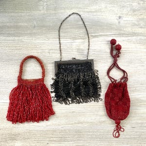 May include: Three small handbags: a red beaded pouch with a fringe, a black beaded rectangular bag with a metal frame and fringe, and a dark red drawstring pouch with beaded texture and two decorative spheres at the top of the cord.