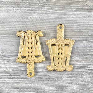 May include: Two antique cast iron trivets in a light yellow color. The trivets are shaped like a bell and a basket with intricate designs.