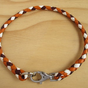 Puede incluir: Un collar de perro de cuero trenzado en marr&oacute;n, blanco y naranja con un cierre plateado.