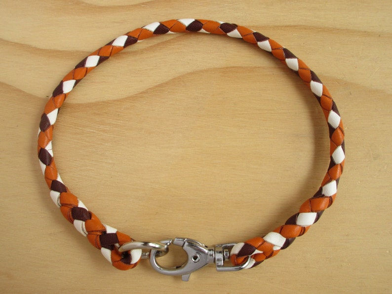 Puede incluir: Un collar de perro de cuero trenzado en marr&oacute;n, blanco y naranja con un cierre plateado.