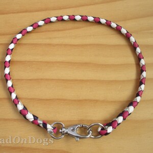 Puede incluir: Un collar de perro de cuero trenzado en rosa, blanco y negro con un cierre plateado.