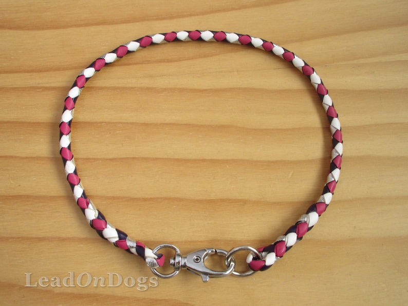 Puede incluir: Un collar de perro de cuero trenzado en rosa, blanco y negro con un cierre plateado.