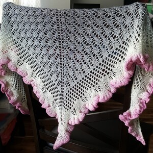 Könnte beinhalten: Ein weißer und rosa gehäkelter Schal mit einem Spitzenmuster und einem gewellten Rand.