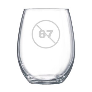 Könnte beinhalten: Ein klares, stieloses Weinglas mit rundem Körper. Das Glas hat eine graue Grafik der Zahl 67 in einem Kreis mit einem Strich hindurch. Das Glas ist leer und steht auf weißem Hintergrund.