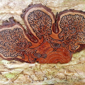 May include: A wooden artwork depicting a tree design with two birds. The piece is carved into a natural wood slice, displaying the tree's branches and the birds in a detailed, rustic style. The colour palette includes shades of brown and tan.