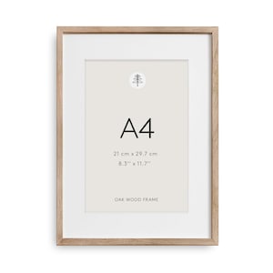 Könnte beinhalten: A4-Eichenholzrahmen mit weißem Passepartout. Der hellbraune, rechteckige Rahmen misst 21 cm x 29,7 cm (8,3" x 11,7"). Der Rahmen hat ein minimalistisches Design mit einem Baumlogo oben.