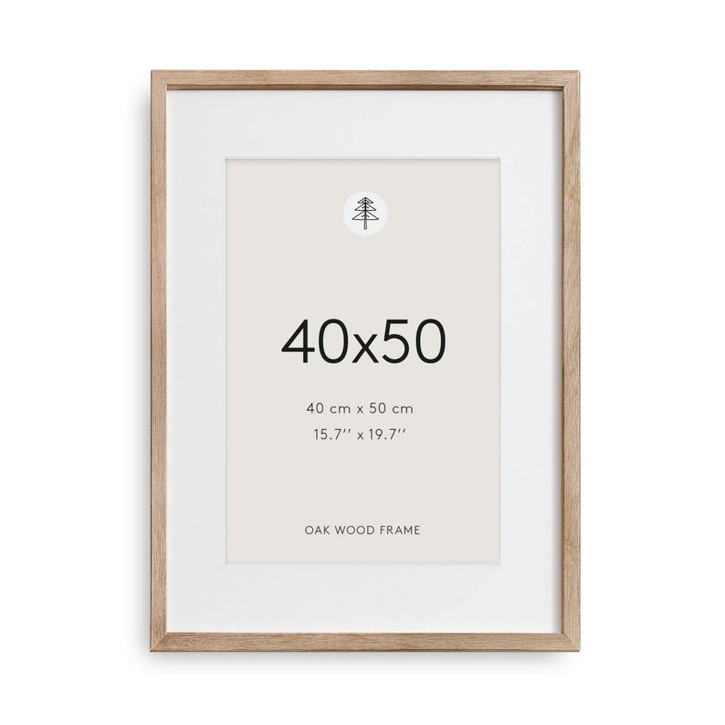 May include: A rectangular oak wood frame with a white mat board. The center displays the text 40x50, 40 cm x 50 cm, 15.7'' x 19.7'', and OAK WOOD FRAME, along with a small circular icon featuring a stylized line drawing of a pine tree.