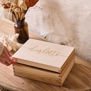 May include: A wooden box with a hinged lid. The lid is engraved with the name "charlotte" in a cursive font.