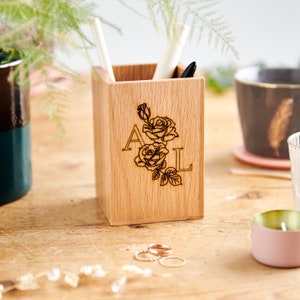 May include: A wooden pencil holder with a personalised design. The holder is engraved with the initials "A L" and a floral design featuring two roses.