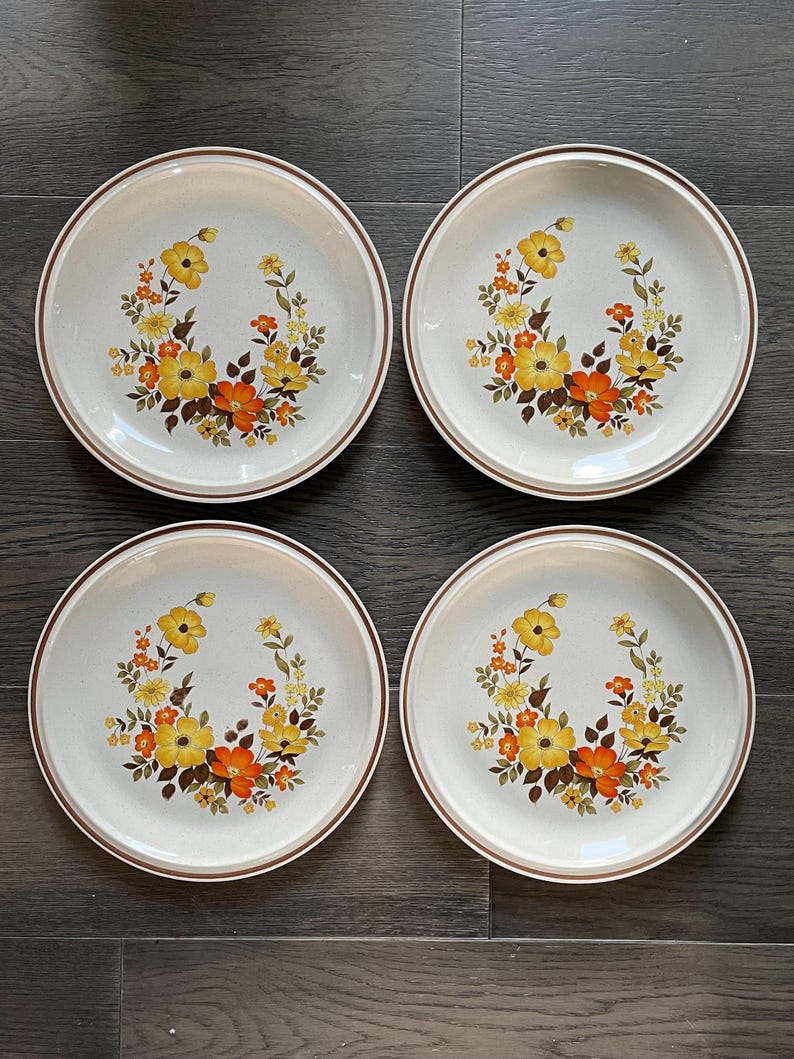 May include: Set of four white ceramic dinner plates with a brown rim and a floral design featuring yellow, orange, and brown flowers.
