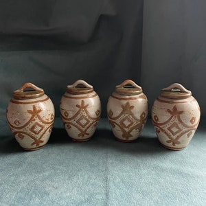 May include: Set of four ceramic canisters with lids. The canisters are white with brown geometric designs.
