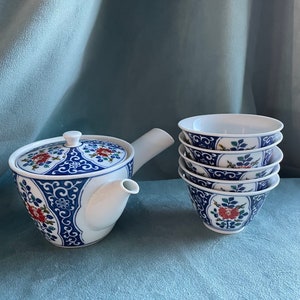 May include: A white teapot with a blue and red floral design and a matching set of four teacups.