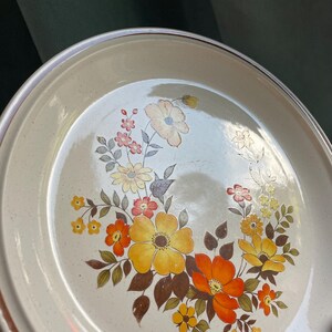 May include: A beige ceramic dinner plate with a brown rim and a floral design featuring yellow, orange, and brown flowers.