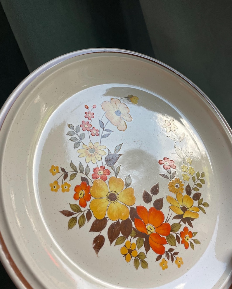 May include: A beige ceramic dinner plate with a brown rim and a floral design featuring yellow, orange, and brown flowers.