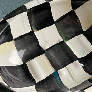 May include: A black and white chequered ceramic serving dish. The dish has a glossy finish and a slightly raised rim. The pattern is a classic checkerboard design, with alternating black and white squares. The dish is oval-shaped.